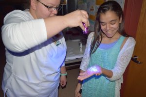 NMCC nursing student Nikki Bouley examines for dirt and germs after “germ gel” is applied to the hands of Kayla Williams, PIMS student. 